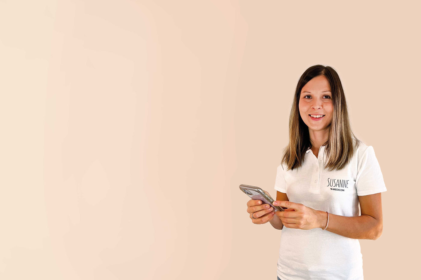 Susanne, die Vitalstoffexpertin von Medicom lächelt in die Kamera und hält ein Handy in der Hand.