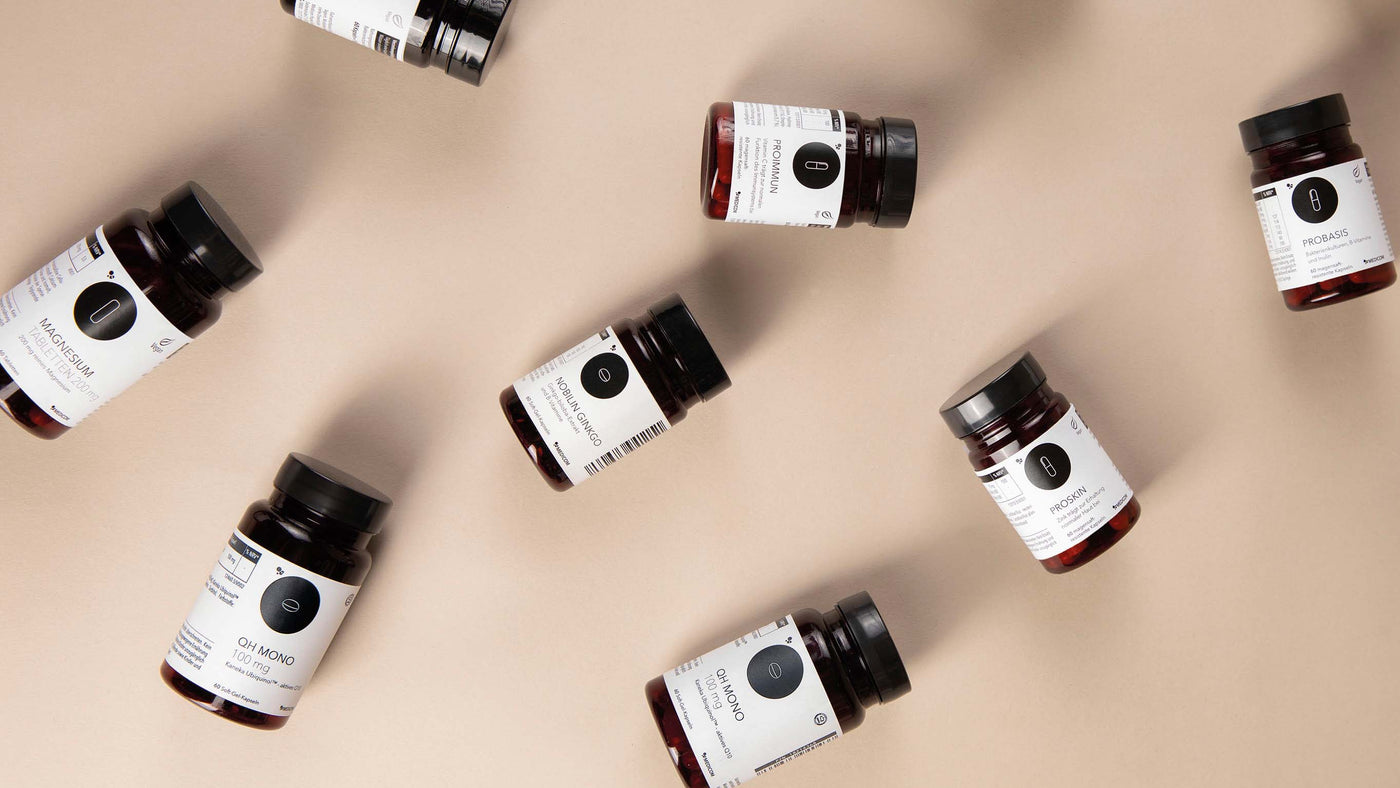 Acht Ergänzungsflaschen mit weißen Etiketten sind auf einem beigen Hintergrund verstreut.