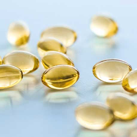 Nahaufnahme von mehreren durchscheinenden gelben Gelkapseln, die auf einer hellen Fläche verstreut sind.