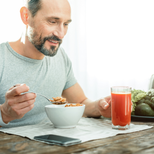 Ein Mann sitzt beim Frühstück und isst ein Müsli. Vor ihm steht ein Glas Obstsaft