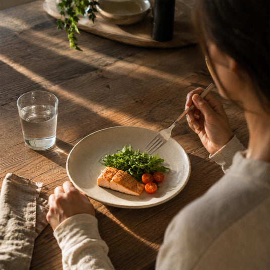 Eine Frau isst Lachs, Salat und Tomaten.