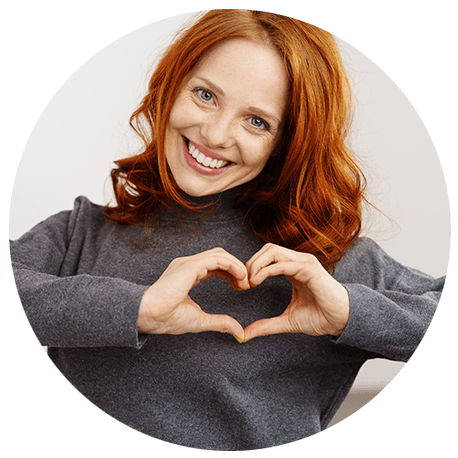 Eine junge, rothaarige Frau formt ein Herz mit ihren Händen