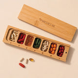 Die „Medicom Kapselbox“ von Medicom ist ein Tablettenbehälter aus Holz mit sieben Fächern, die jeweils mit verschiedenfarbigen Kapseln und Tabletten gefüllt sind.