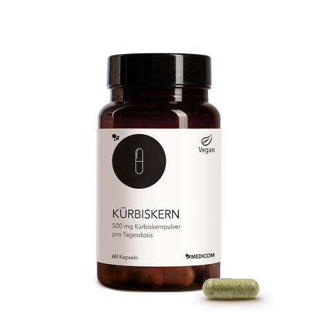 Die Kürbiskern-Produktdose von Medicom in der Vorderansicht und eine Kapsel Kürbiskernpulver im Vordergrund