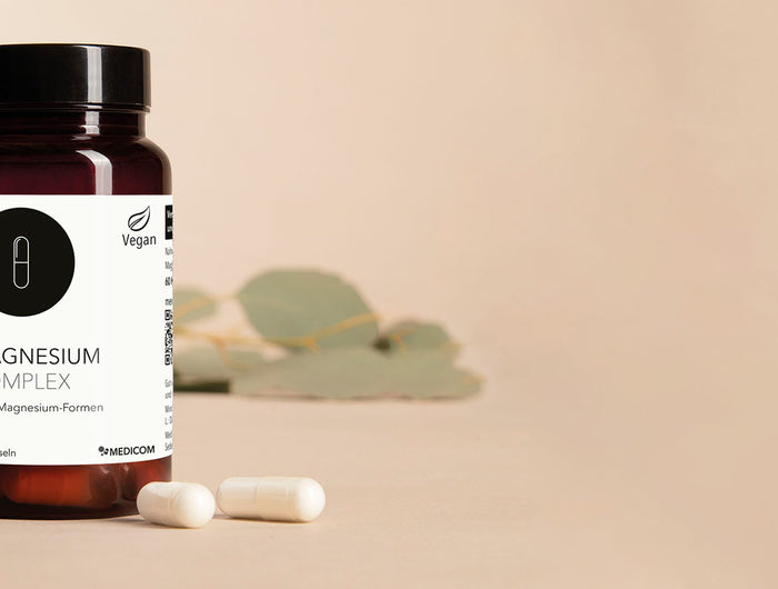 Die Produktdose von Magnesium Complex mit zwei Kapseln im Vordergrund. Im Hintergrund eine Schale mit Kapseln.