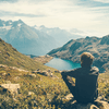 Ein Mann sitzt auf einer Berganhöhe und blickt auf einen Bergsee