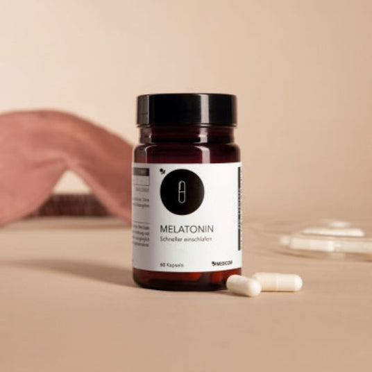 Eine Flasche Melatonin-Kapseln mit zwei Kapseln daneben auf einer beigen Fläche und einem beigen Hintergrund.