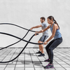Eine junge Frau und ein junger Mann beim Fitnesstraining mit schwarzen battle ropes
