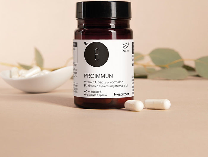 Die Produktdose von ProImmun und zwei Kapseln im Vordergrund