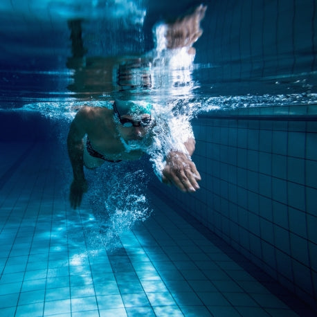 Ein Schwimmer im Schwimmbad unter Wasser mit Taucherbrille und mit Badekappe