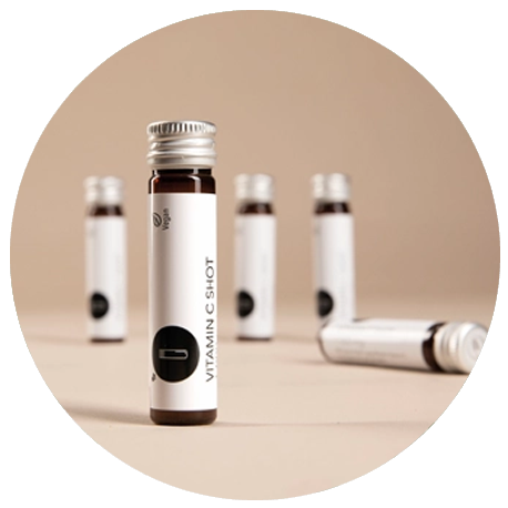 Fünf kleine braune Flaschen mit der Aufschrift Vitamin C Shot sind auf einer beigen Fläche mit beigem Hintergrund angeordnet.