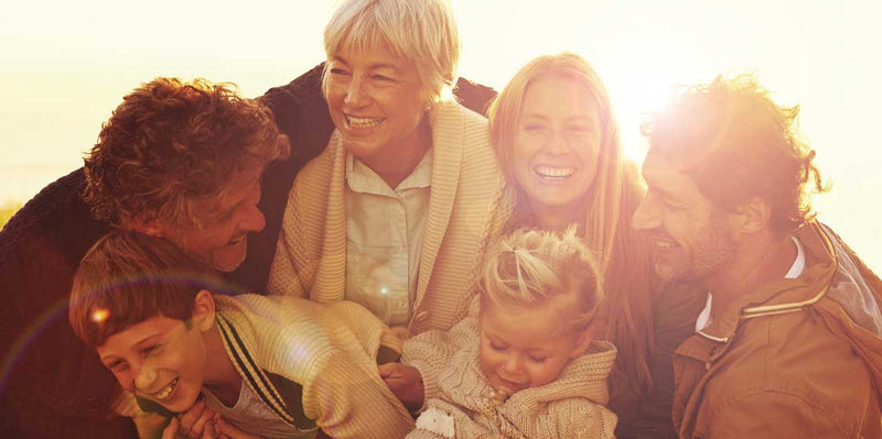 Eine glückliche sechsköpfige Familie lächelt und lacht im warmen Sonnenlicht.
