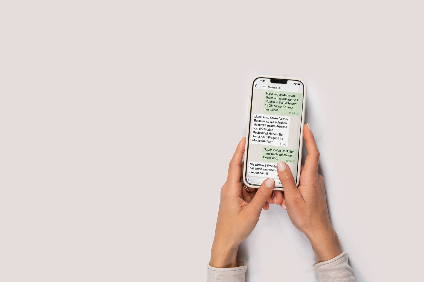 Hände, die ein Smartphone halten, das ein Chat-Gespräch auf Deutsch auf hellem Hintergrund anzeigt.