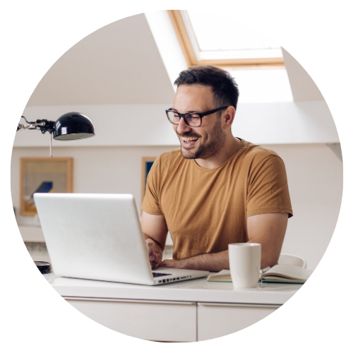 Ein Mann sitzt am Laptop und lacht in die Laptopkamera