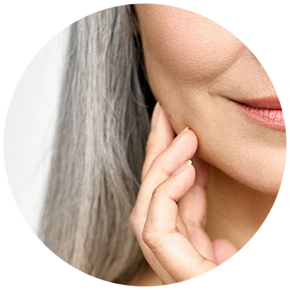 Nahaufnahme einer Person mit langen grauen Haaren, die ihre Wange berühren, mit glatter Haut und einem leichten Lächeln.