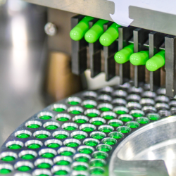 Grüne Kapseln werden von einer automatischen Maschine in einer pharmazeutischen Produktionslinie sortiert.