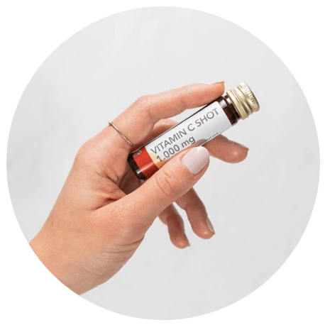 Eine Hand hält ein kleines Fläschchen mit der Aufschrift Vitamin C Shot 1.000 mg vor einem hellen Hintergrund.