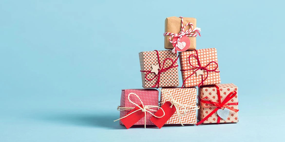 Ein Stapel von sechs Geschenkkartons, eingewickelt in rotes, weißes und braunes Papier mit dekorativen Bändern und Anhängern.