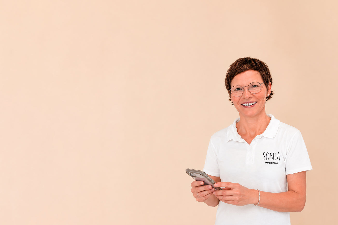Sonja, die Vitalstoffexpertin von Medicom lächelt in die Kamera und hält ein Handy in der Hand.