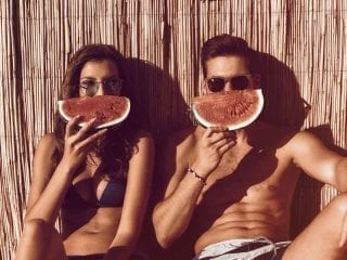 Junges Paar hält Wassermelonenstücke vor das Gesicht