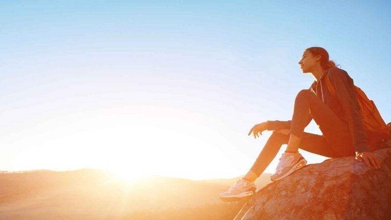 Eine Frau sitzt auf einer Bergkuppe und genießt die Landschaft und den Sonnenschein