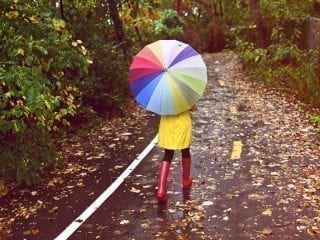 Junge Frau geschützt mit Regenmantel, Regenstiefeln und Regenschirm