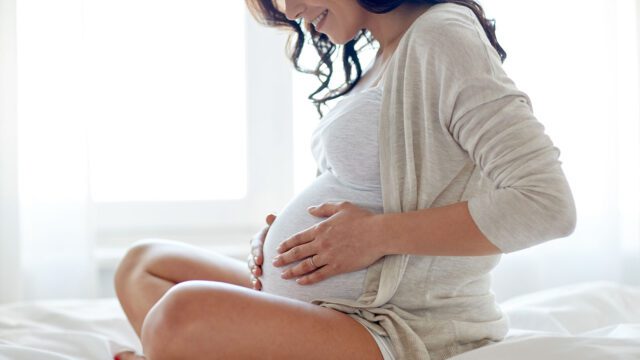 Schwangere Frau hält sich Hände an den Bauch