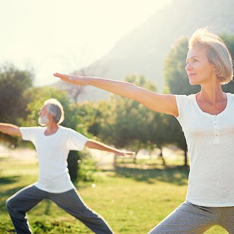 Eine Frau und ein Mann mittleren Alters machen eine Yogaübung im Park