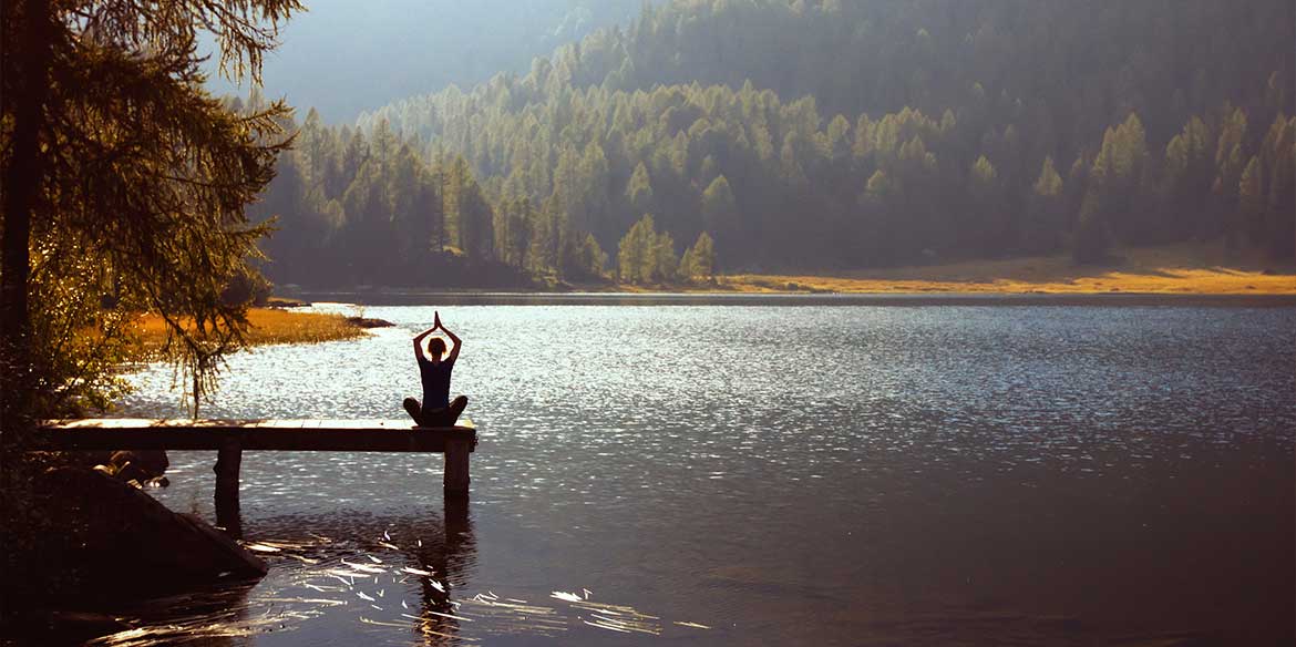 Eine Frau am See auf einem Steg bei einer Yogaübung