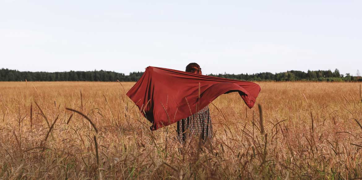 Eine Frau läuft mit einem dunkelroten Tuch durch ein Weizenfeld