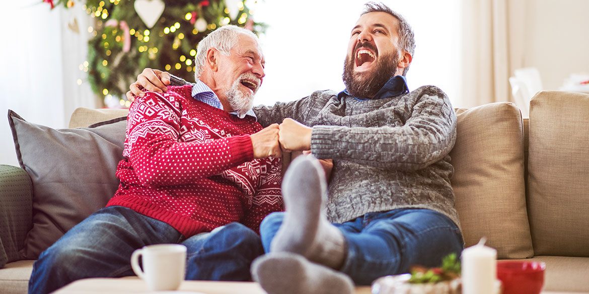 Vater und Sohn lachen zusammen auf dem Sofa. Im Hintergrund ein Weihnachtsbaum