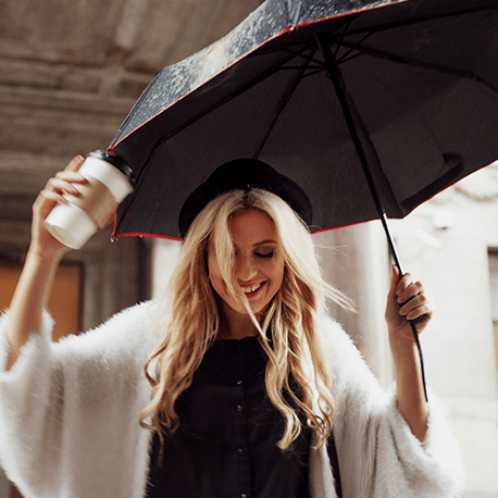 Eine Frau tanzt im Regen mit Regenschirm und Coffee-To-Go-Becher