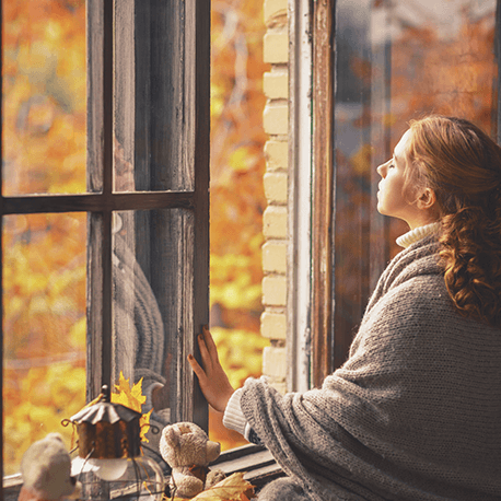 Eine Frau steht vor einem geöffneten Fenster mit geschlossenen Augen.