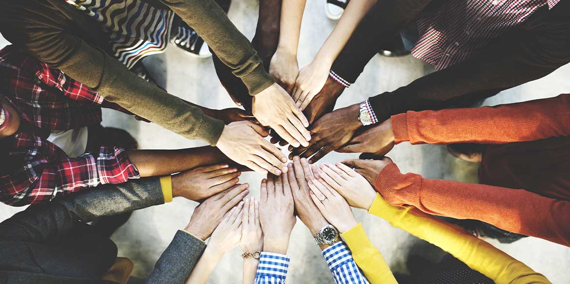 Eine Gruppe von Menschen mit verschiedener Hautfarbe hält Hände in die Mitte. 