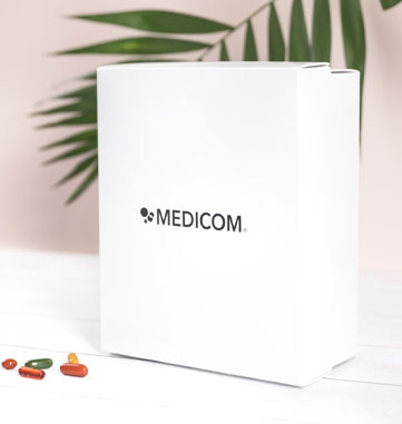Die weiße Medicom Box mit Palme im Hintergrund und im Vordergrund bunte Pillen