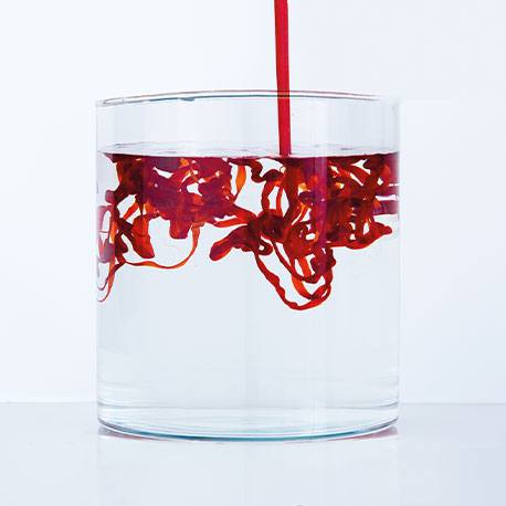 Ein Glas Wasser mit Krillöl, das hineinfließt und sich mit Wasser vermischt.