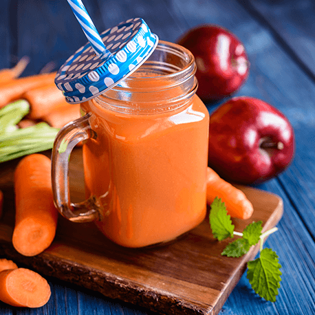 Karotten-Smoothie mit Karotten und Äpfel im Hintergrund