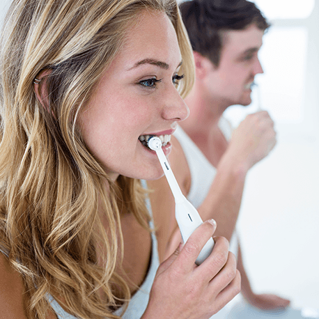 Eine junge Frau und ein junger Mann putzen sich mit einer elektrischen Zahnbürste die Zähne