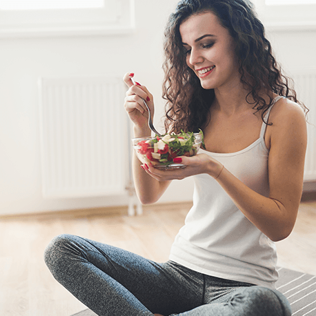 Junge Frau in Sportleggings isst einen Salat im Schneidersitz