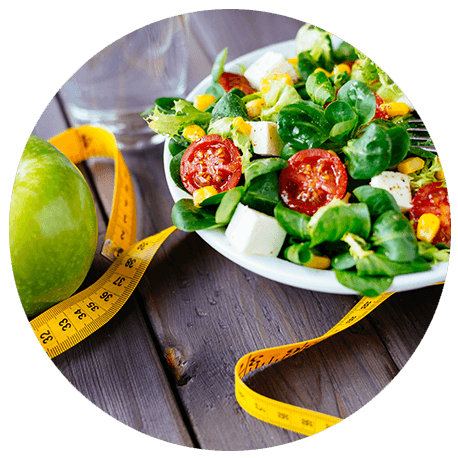 Gemischter Feldsalat, ein grüner Apfel und ein gelbes Maßband auf einem Holztisch. Bewusst ernähren – Gewicht kontrollieren