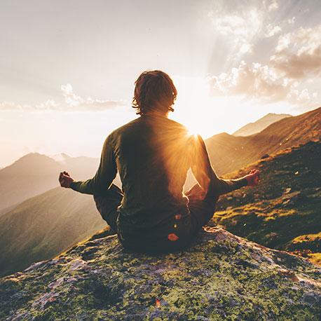 Meditierender Mann in einer Berglandschaft bei Sonnenaufgang