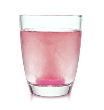 Elektrolyt Brausetablette löst sich in einem Glas Wasser auf und färbt es rosa