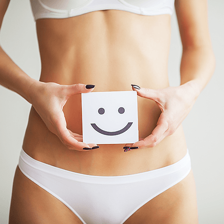 Oberkörper einer Frau in weißer Unterwäsche. Die Frau hält eine  Karte mit einem Smiley vor den Bauchnabel