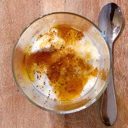Ein Glas mit Naturjoghurt, Honig und Propolis und ein Löffel aus einem Holztisch