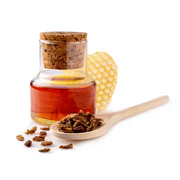 Ein Honigbehälter, Propolisstücke auf einem Holzlöffel und ein Stück Bienenwaben
