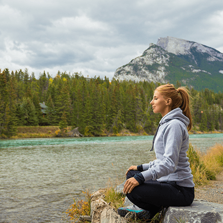 Frau sitzt am Ufer im Schneidersitz in Yogahaltung und meditiert