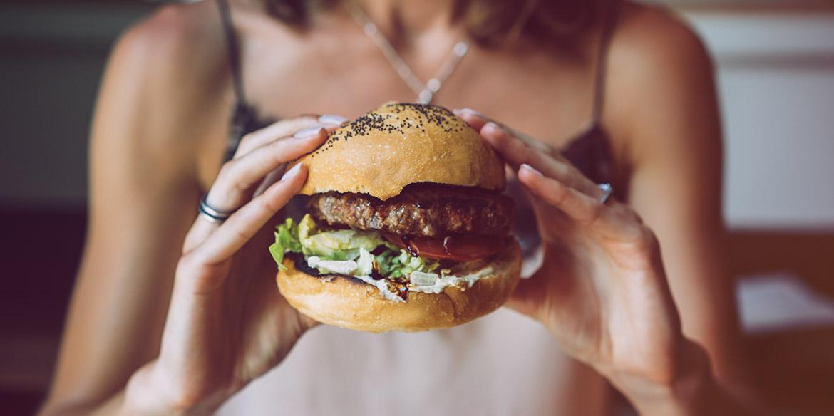 Frau hält vollen, fetten Burger in der Hand