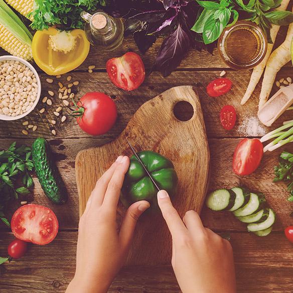 Holztisch mit verschiedenen Gemüse (Tomaten, Gurken, grüne Paprika, Salat), Frischkräutern, Reis und Mais