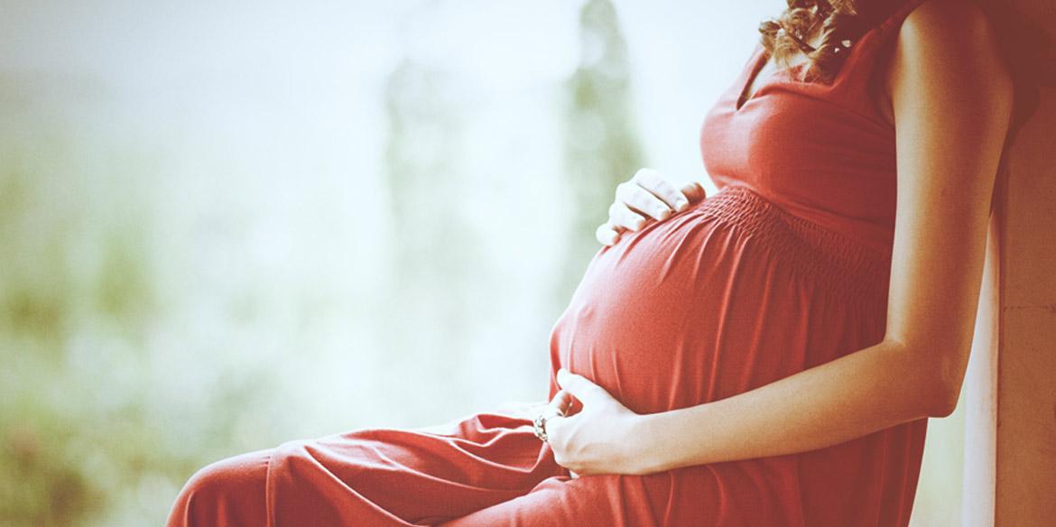 Schwangere Frau im roten Kleid hält sich den Bauch