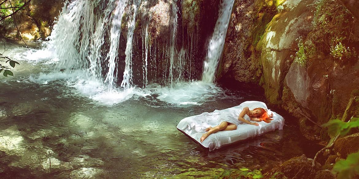 Eine Frau liegt auf einer Luftmatratze im Wasser neben einem Wasserfall.